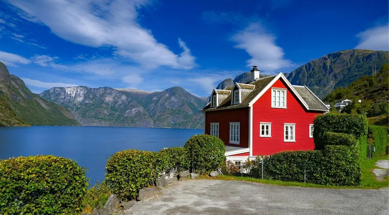 A red Norwegian house above a calm blue fjord with mountains behind