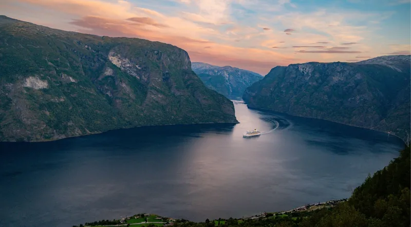 A cruise boat sailing a wide Norwegian fjord at dusk